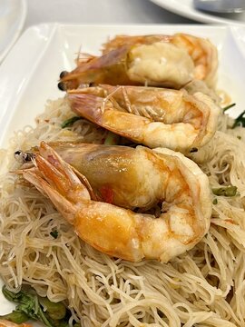 a photography of a plate of noodles with shrimp and greens, there are three shrimps on top of a plate of noodles.