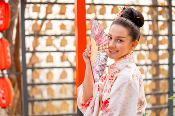 Portrait of pretty young woman wear japanese style dress and hold fan also look at camera in front of row of lantern.