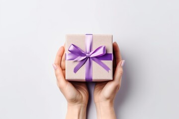 A woman's hands holding a gift box with a purple ribbon