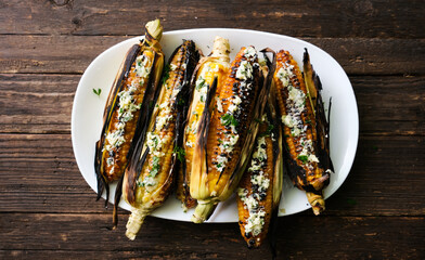 Grilled corn cobs with butter, cheese and herbs, on a dark wooden background. Top view.