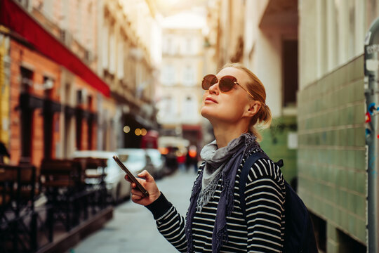 A young female traveler walks through the streets of a European city using a smartphone. Blonde in dark glasses and with a backpack, independent walks to the sights