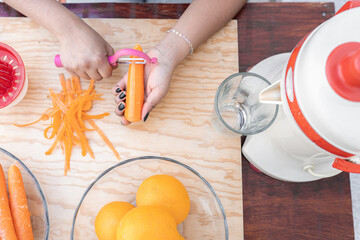 A young Hispanic woman is peeling some carrots to make orange and carrot juice using a vintage squeezer