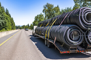 Day cab white big rig semi truck transporting plastic pipes on the long flat bed semi trailer...