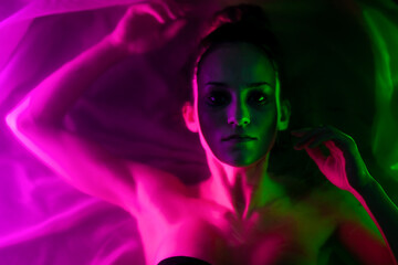 Beautiful wet girl in bikini lying in water portrait. Sidelit with neon lights..