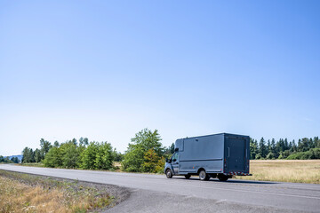 Small rig semi truck with huge box trailer making delivery running on the narrow winding road with summer meadows on the sides