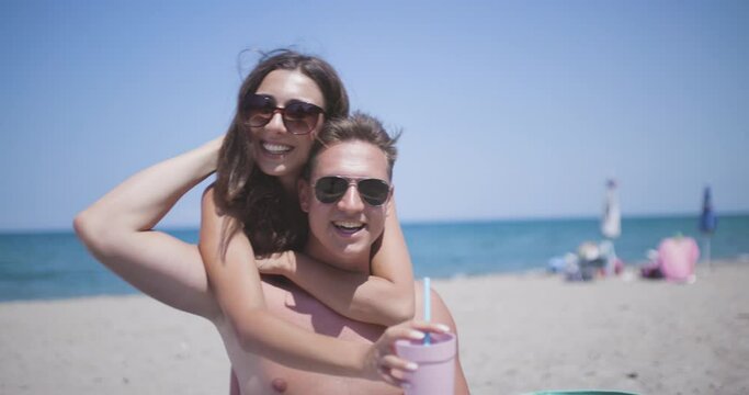 Couple in love on a sand beach singing and hugging each other. Lovely young man and woman enjoying summer at sea. Recorded at 50fps