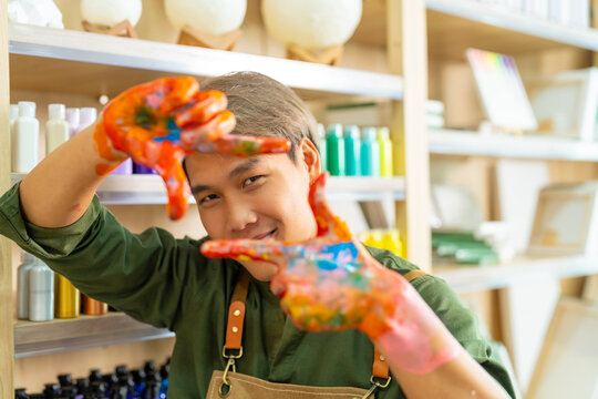 Portrait of Asian generation z man learning acrylic pouring art on canvas workshop at art studio. Young artist university student enjoy and fun creating colorful abstract modern art painting in class.