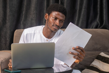 Working with papers. Serious african male entrepreneur work at home office alone hold read document hardcopy think on conditions terms. Focused young man engaged in paperwork edit text of agreement - obrazy, fototapety, plakaty