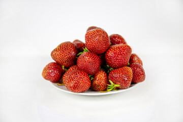 Strawberries of bright red color in a pile on a plate isolated on a white background. Raw organic fruits. Useful products.
