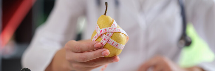 Nutritionist holds pear fruit and measuring tape in his hand and advises to eat healthy food with...
