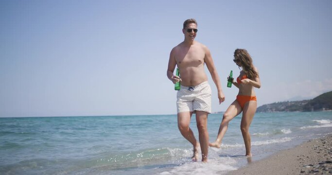 Couple on a sand beach with beer bottles running together. Enjoying summer at sea concept. Recorded at 50fps