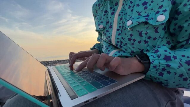 Digital nomad. A woman typing on a laptop in close-up, sitting on a sandy beach and working at a laptop, typing a code or answering an email. High quality 4k footage