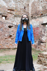 Naklejka premium Woman wearing gas mask with spikes in blue jacket and black dress standing in ruined building