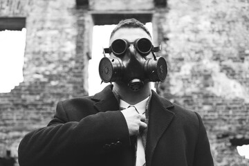 A man in a black coat, business suit, gas mask and steampunk goggles. Black and white photo