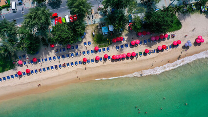 Fototapeta na wymiar View from above of the clear sea water with tourists enjoying the beach on sun bed with red umbrella in Patong beach