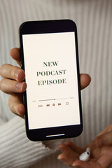 Unrecognizable woman holding mobile phone NEW PODCAST EPISODE listening website page app application with wireless headphones. Audio healing, sound therapy wellness rituals, positive mental health