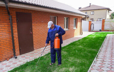 A man works in the garden, spraying weeds from a sprayer.