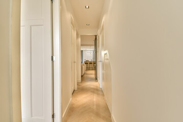 an empty hallway with white walls and wood flooring, leading to the living room on the right...