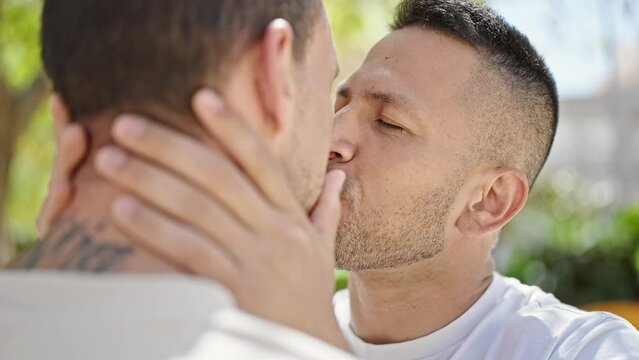 Two men couple standing together kissing at park