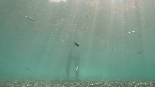 Underwater view of fish hook by fisherman fishing on standing at the seashore mediterranean sea.
