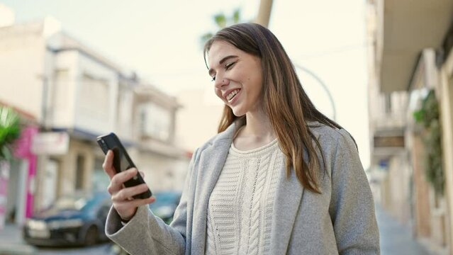 Young hispanic woman using smartphone smiling at street