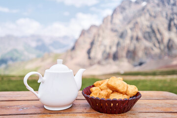 Teapot with tea and delicious National Kazakh pastries baursak. Street cafe in the highlands with a view of the mountains.. Fry dough in boiling oil in a frying pan.