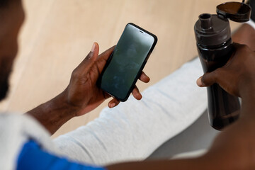 Hands of african american man sitting on mat and using smartphone at home