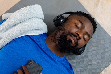 African american man with headphones and smartphone lying on mat at home