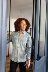 Happy caucasian man with curly hair welcoming at door at home
