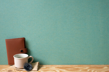 Diary notebook and cup of tea with dry flower on wooden desk. green wall background. copy space