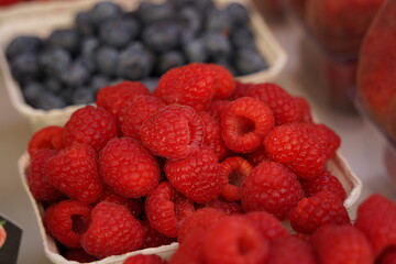 Small paper boxes with  raspberries and  blueberries displayed on food market