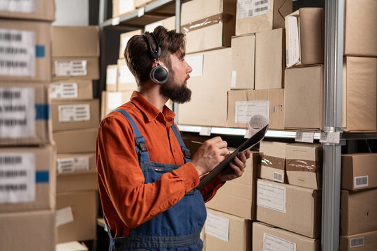 Warehouse manager wearing headset writing on clipboard working in a large warehouse checking checklist - Powered by Adobe