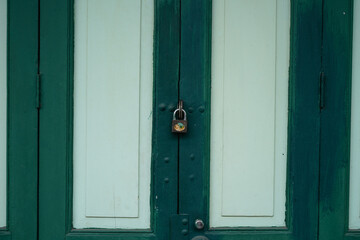 The door of an ancient house is made of wooden panels connected to hinges, painted in green.