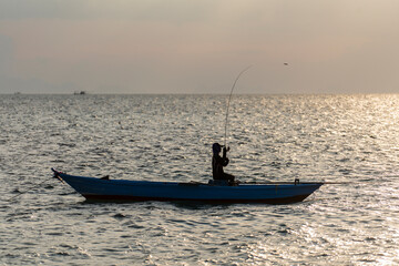 Silhouette of thai fisherman in a boat on the sea water at beautiful sunset background, island Koh Phangan, Thailand
