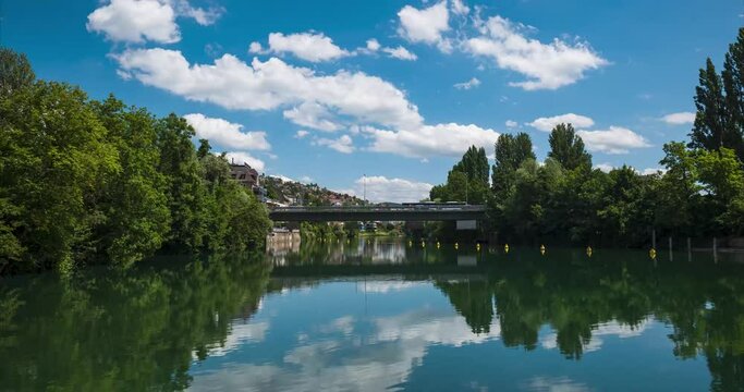 Limmat river flowing under Europe bridge in Zurich city Switzerland time lapse. Low angle view, sunny summer day, traffic moving on the bridge, puffy passing clouds, yellow buoys floating on the river