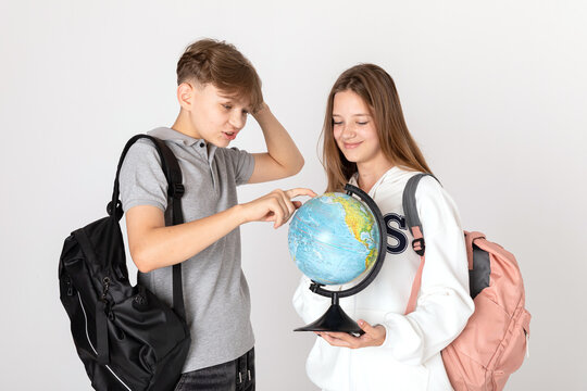 Two schoolchildren, teenagers are looking with interest at the small globe. Using a large magnifying glass to see the smallest details. Studying geography together.