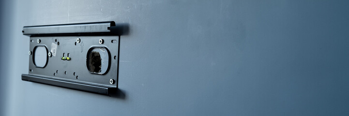 A TV hanger on a gray blue wall, television suspension system placed in front of a hole. No tv, no more télévision. Space for text on right.