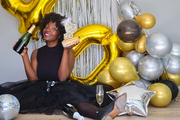 African woman smiling with a champagne bottle and cake celebrating her 40 birthday in a party.