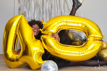 African woman in a 40 birthday party playing with 40 birthday golden balloons on the floor.