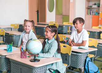 Elementary School and People Concept. Diverse excited group of emotional happy junior school kids sitting at desks in classroom