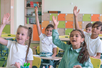 Group of Multi-ethnic happy elementary school children raising their arms to answer asian teacher question in classroom. Education, elementary school, learning, Back to school concept