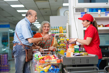 Indian senior couple checkout from super market,goods scanning by female cashier at super market.