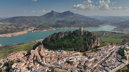 Flying over the orange roofs of the town, fortress on the mountain and the view of the river in Zahara de la sierra. - 628403179