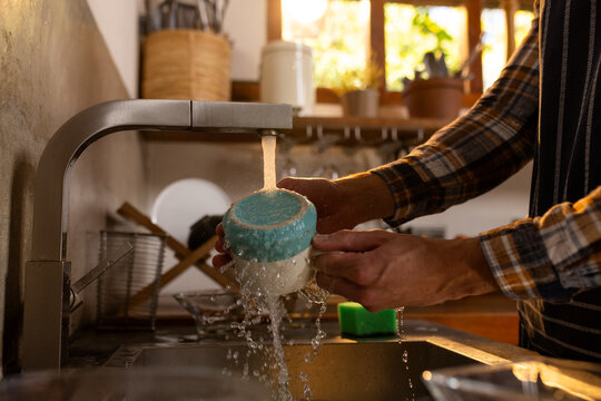 Midsection of indian man washing dishes in sunny kitchen at home