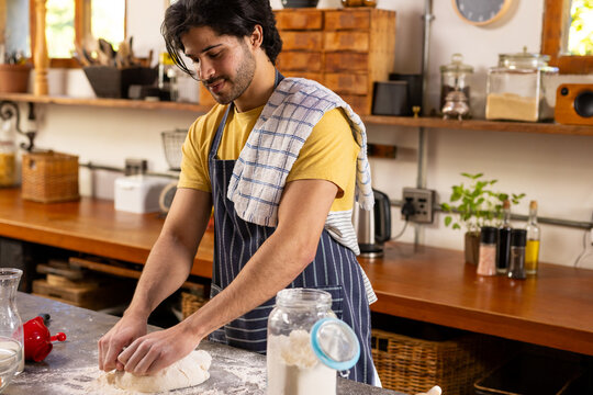 Indian man in apron preparing bread dough in sunny kitchen at home