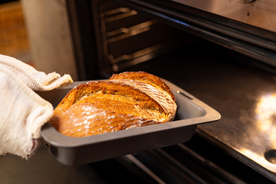 Hands of indian man in apron taking bread out from oven in kitchen