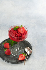 Strawberry granita or fresh berry sorbet in glass on old  grey table background. Texture of ice cream or sorbet. Ice cream with strawberry and mint. Sorbet recipe. Summer treat. Selective focus.