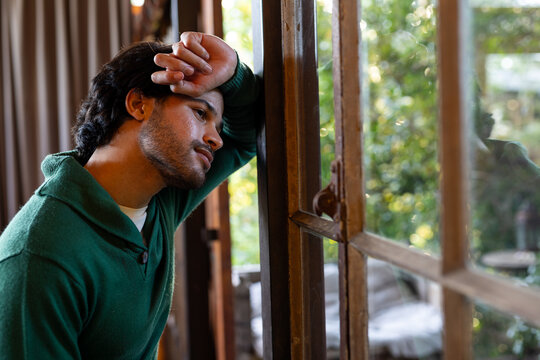 Thoughtful indian man looking out window at sunny home