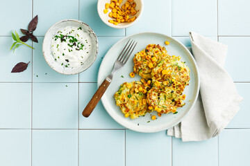 Zucchini and corn fritters with sour cream and herbs. Top view, flat lay.