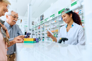 Happy Chinese pharmacist assists senior couple who is buying prescription medicine in pharmacy.